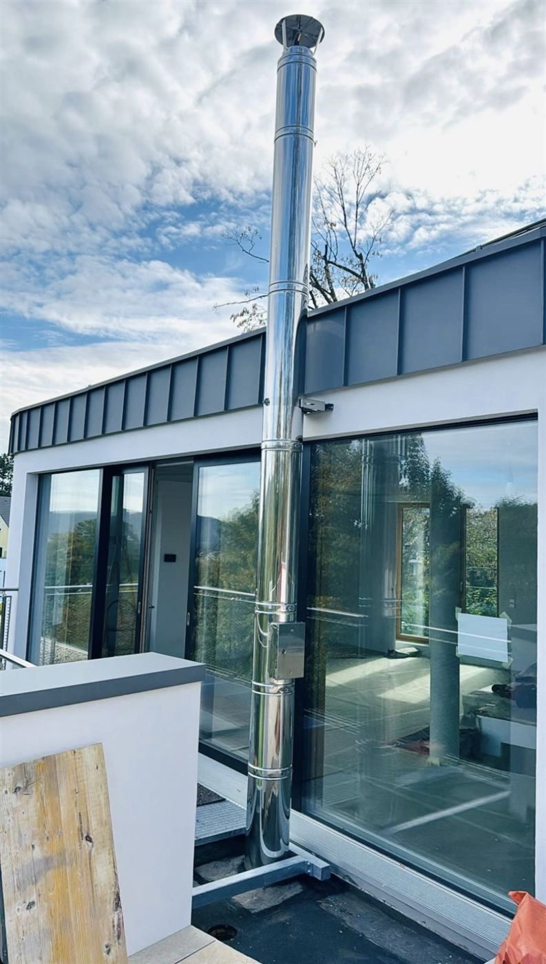 Edelstahl-Außenwandkamin an moderner Glasfassade eines Flachdachhauses