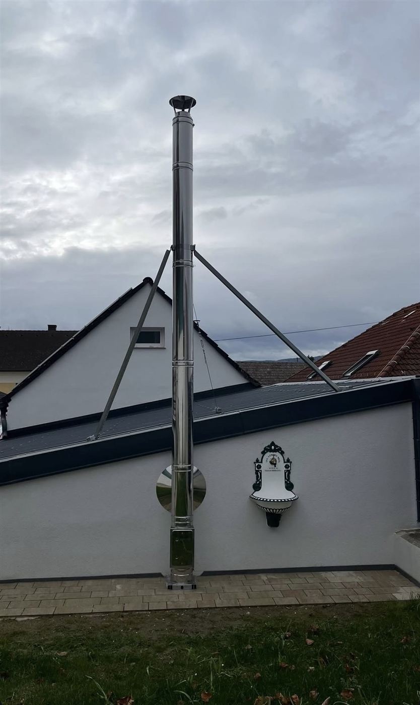 Freistehender Außenwandkamin mit Abspannstreben an weißer Hausfassade