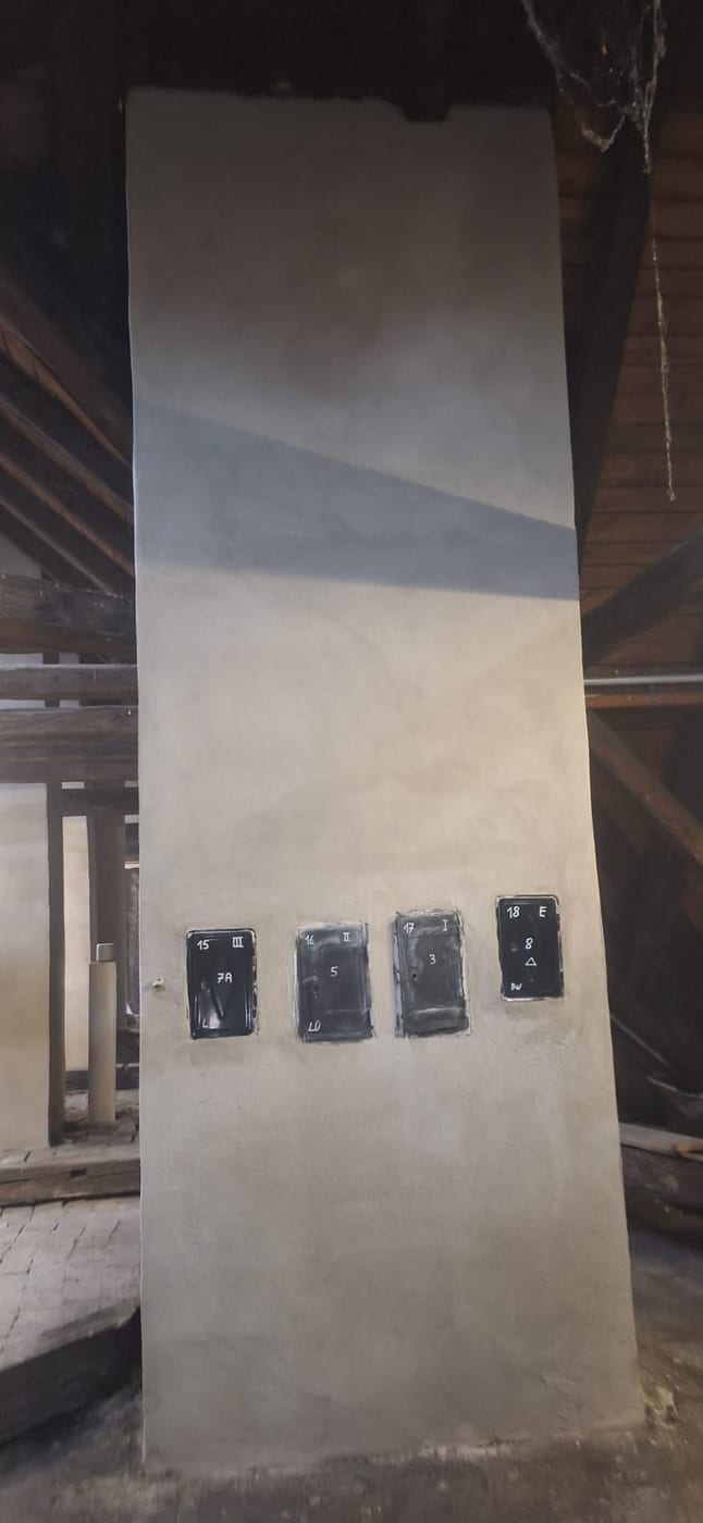 Fertig verputzte Wangenmauer mit vier Kamintüren im Dachboden